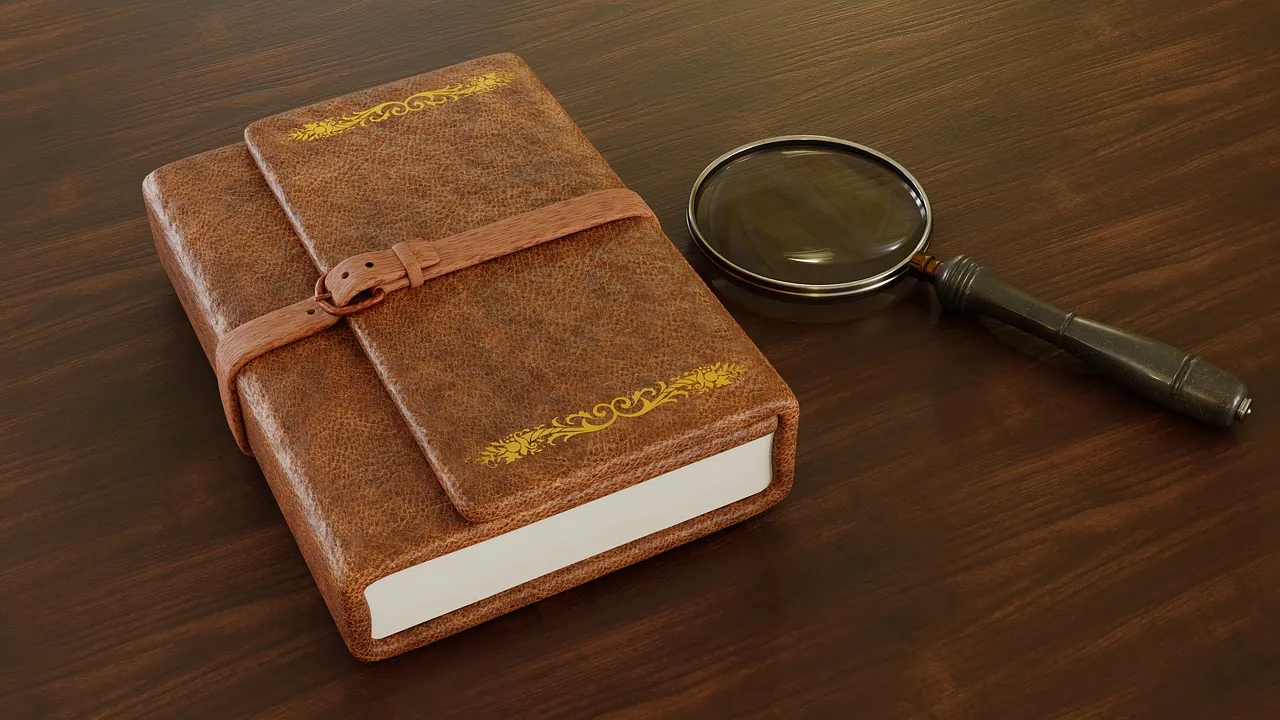 Un carnet de cuir fermé par sa lanière et une loupe posée à côté